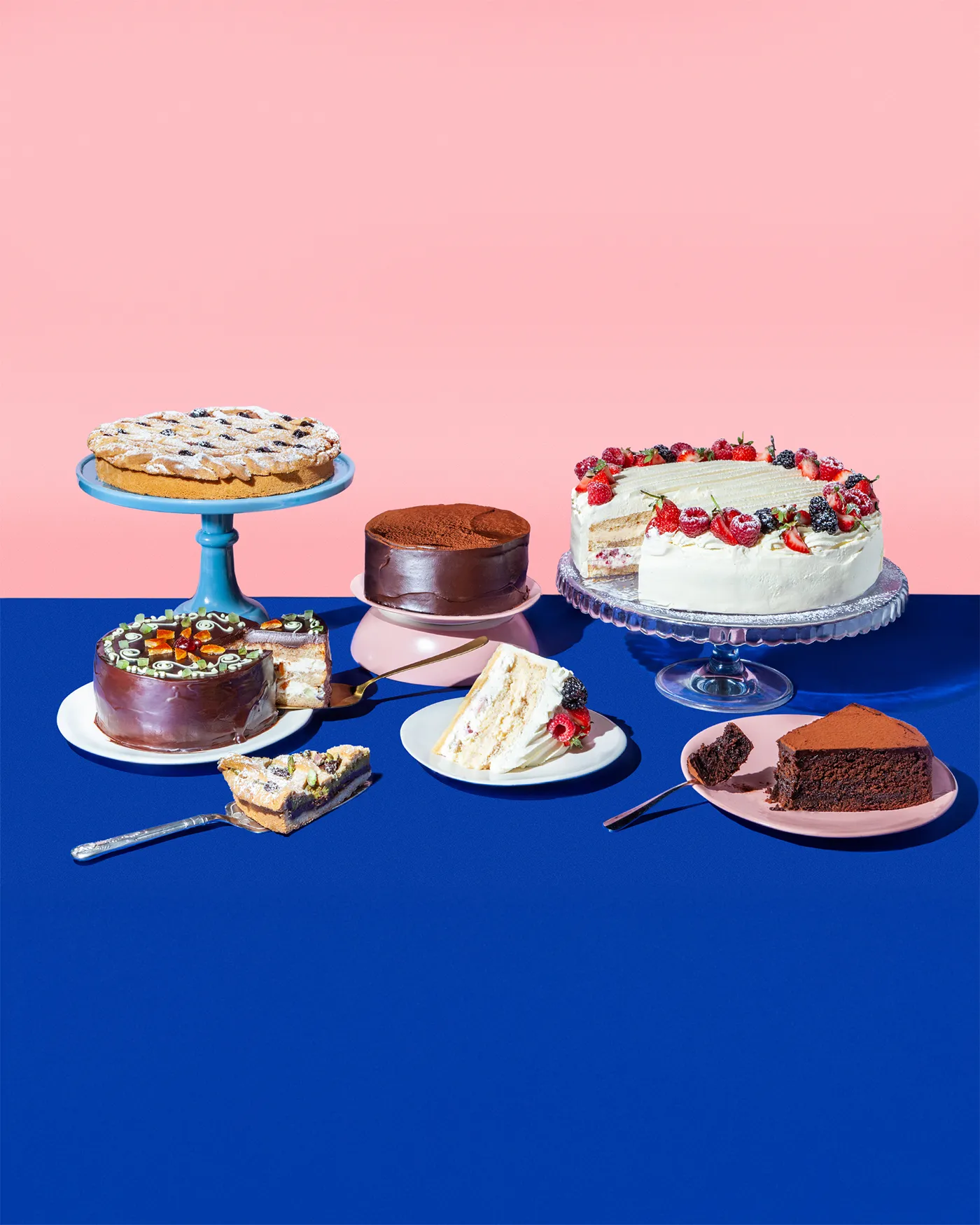 Spread of cakes and tarts on pink and cobalt, including a berry layer cake and a chocolate torte