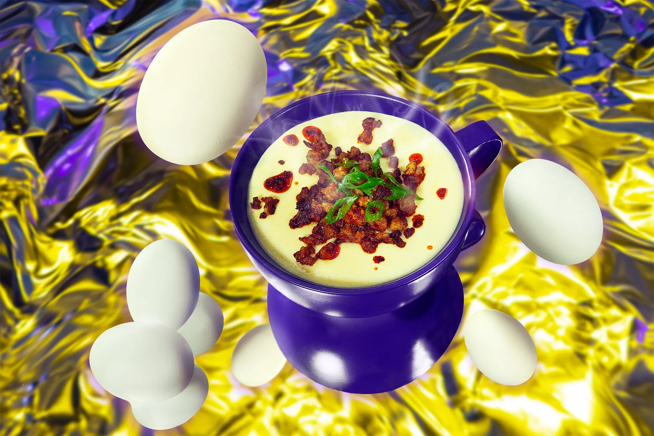 Creamy eggs in a purple pot topped with crisp chorizo and spring onion, whole eggs floating over gold foil